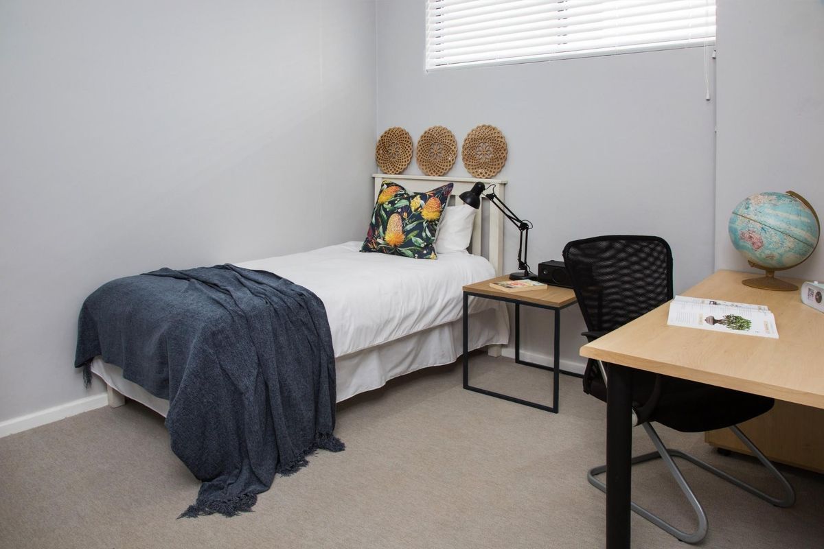 A well-maintained bedroom featuring neutral wall tones and venetian blinds, providing a clean and functional space.