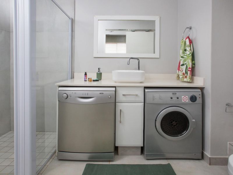 A functional bathroom featuring a shower enclosure, a vanity with a vessel sink, and integrated space for laundry appliances.