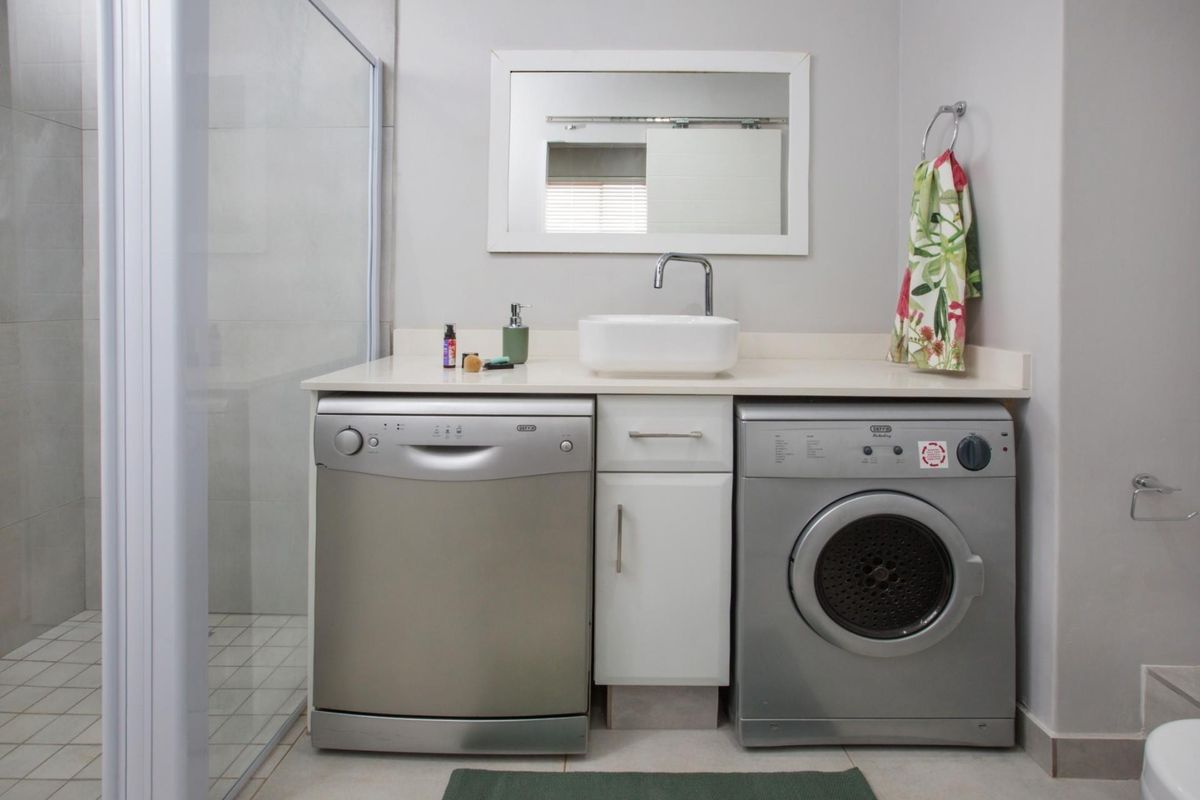 A functional bathroom featuring a shower enclosure, a vanity with a vessel sink, and integrated space for laundry appliances.