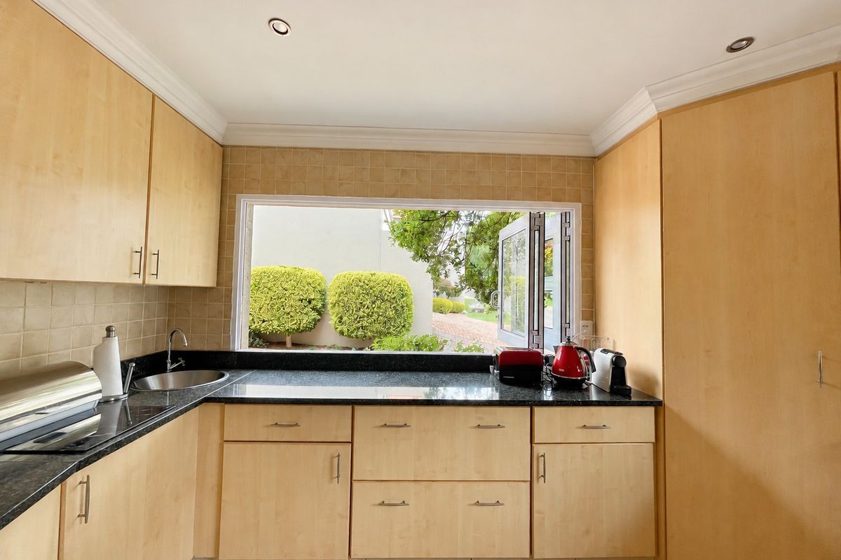 A functional kitchen featuring light-wood cabinetry, granite countertops, and a large window overlooking the garden, providing ample natural light and workspace.