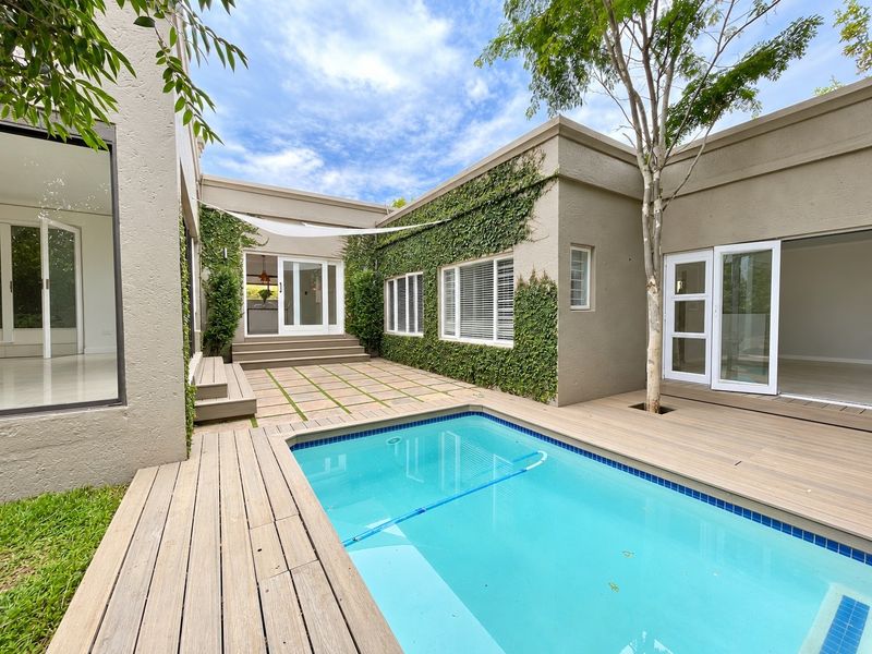 A well-maintained courtyard featuring a swimming pool, timber decking, paved patio area, and lush climbing ivy on the exterior walls.