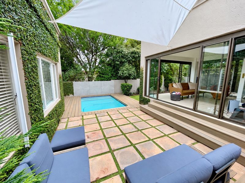 A well-maintained outdoor pool area featuring timber decking, stone paving, and seamless indoor-outdoor flow through large sliding glass doors.