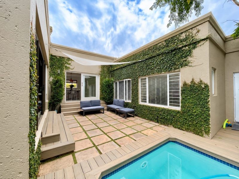 A private courtyard featuring a swimming pool, timber decking, and a paved patio area, surrounded by ivy-covered walls and direct access to the home.