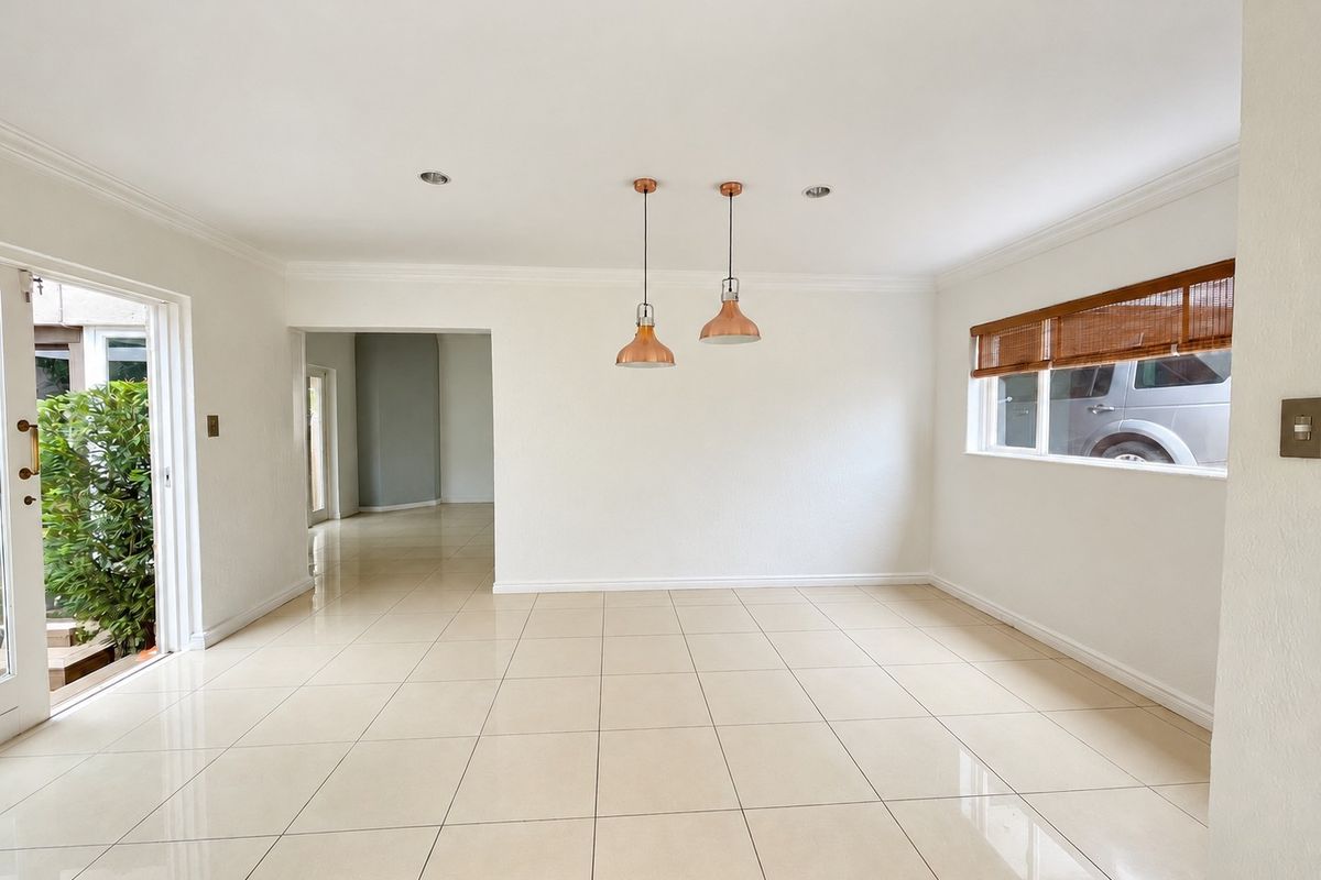 A bright, open-plan living area featuring neutral tiled flooring, modern pendant lighting, and direct access to the outdoor space through a sliding glass door.