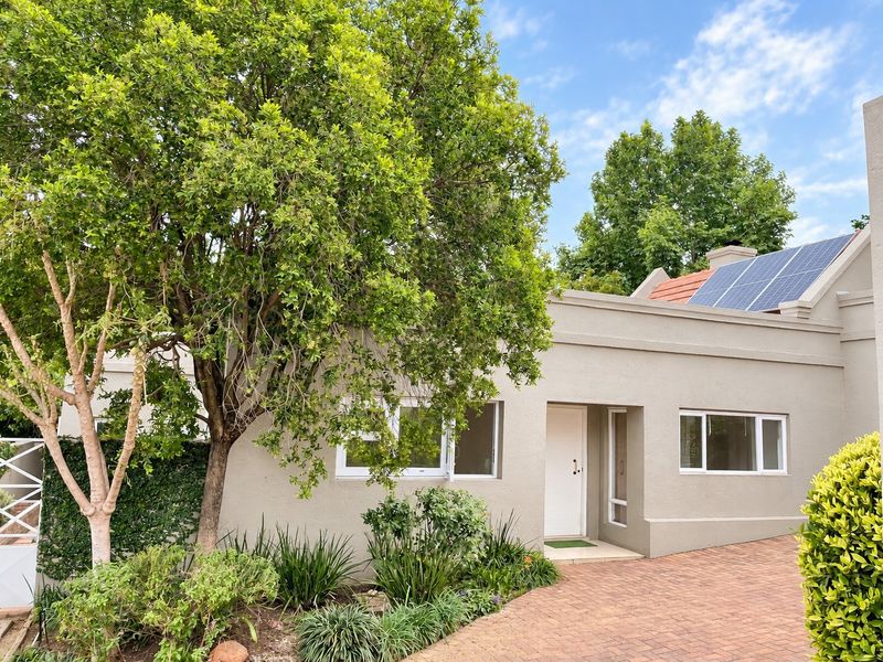 Front elevation of a well-maintained house featuring a paved driveway, established garden, and roof-mounted solar panels.