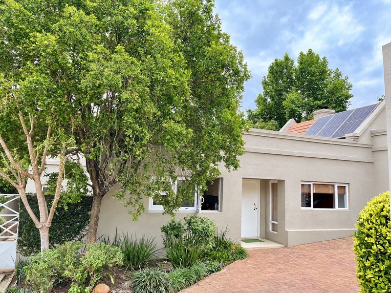 Front elevation of the house featuring a paved driveway, plastered exterior walls, aluminium window frames, and roof-mounted solar panels.