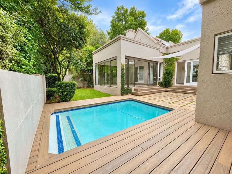 A well-maintained outdoor pool area featuring timber decking, a paved patio, and direct access to the home through large sliding glass doors.