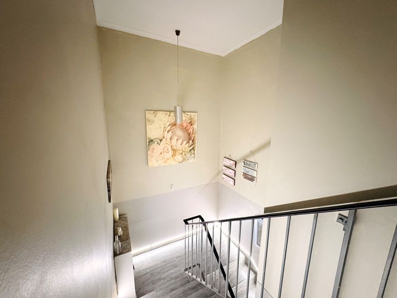 A bright and modern staircase area featuring a metal balustrade, tiled flooring, and contemporary pendant lighting, creating a clean and welcoming transition space.