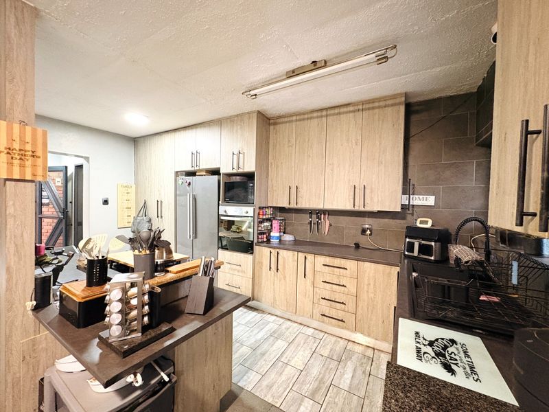 Functional kitchen featuring wood-look cabinetry, dark countertops, built-in oven and microwave, tiled backsplash, and tiled flooring in a townhouse setting.