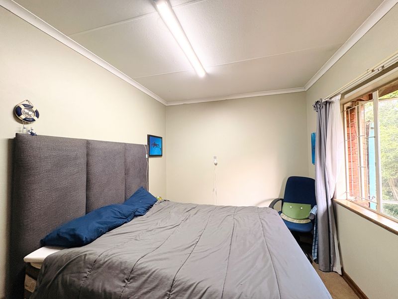 A standard bedroom featuring neutral walls, coving, and a window fitted with security bars, providing functional living space.
