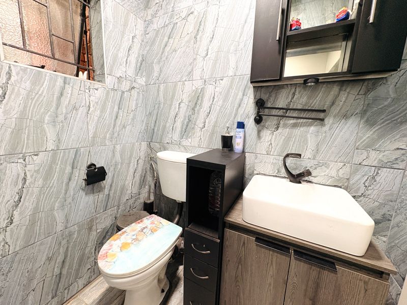 A compact bathroom featuring modern marble-effect wall tiles, a vessel sink with a vanity cabinet, and a wall-mounted medicine cabinet.