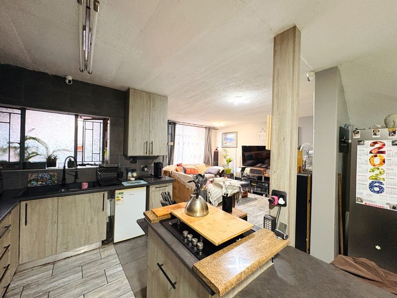 Open-plan living area featuring a functional kitchen with built-in cabinetry, a central island with a hob, and tiled flooring throughout the space.