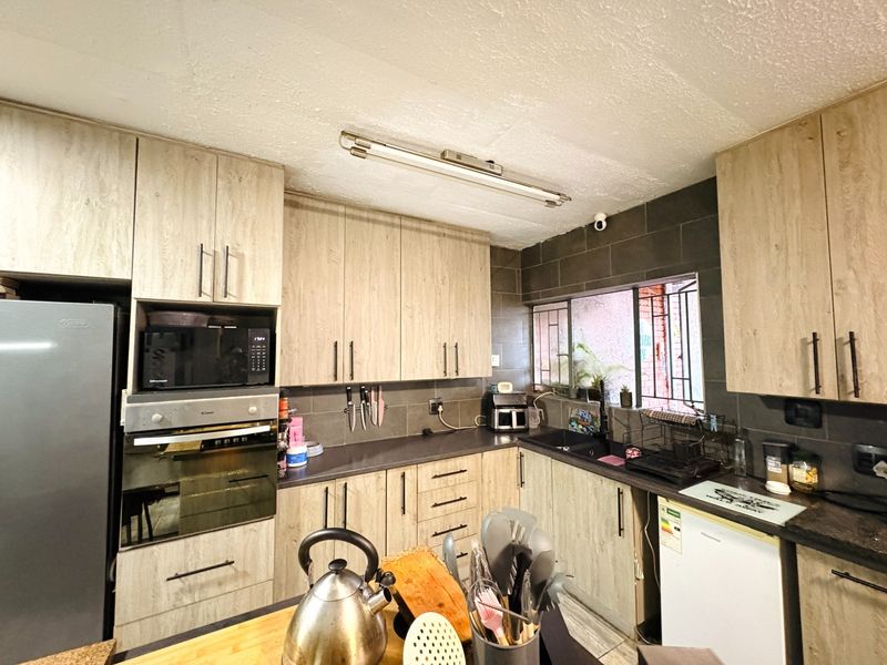 Functional kitchen featuring light wood-grain cabinetry, dark laminate countertops, built-in oven and microwave, and a tiled backsplash with security-barred window.