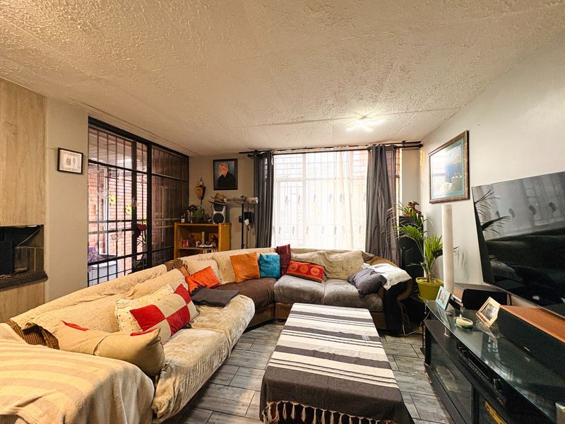 A cozy living room featuring tiled flooring, a built-in fireplace, and a large window with security gate access.