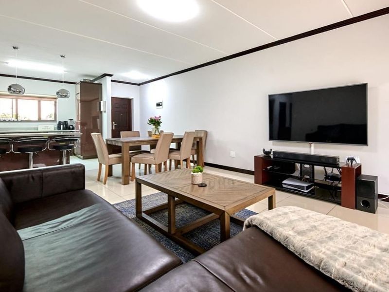 Spacious open-plan living and dining area featuring tiled floors, modern kitchen cabinetry with an island, and integrated lighting throughout the combined space.