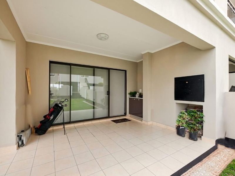 A covered patio area featuring tiled flooring, a built-in braai, and sliding glass doors leading into the apartment.