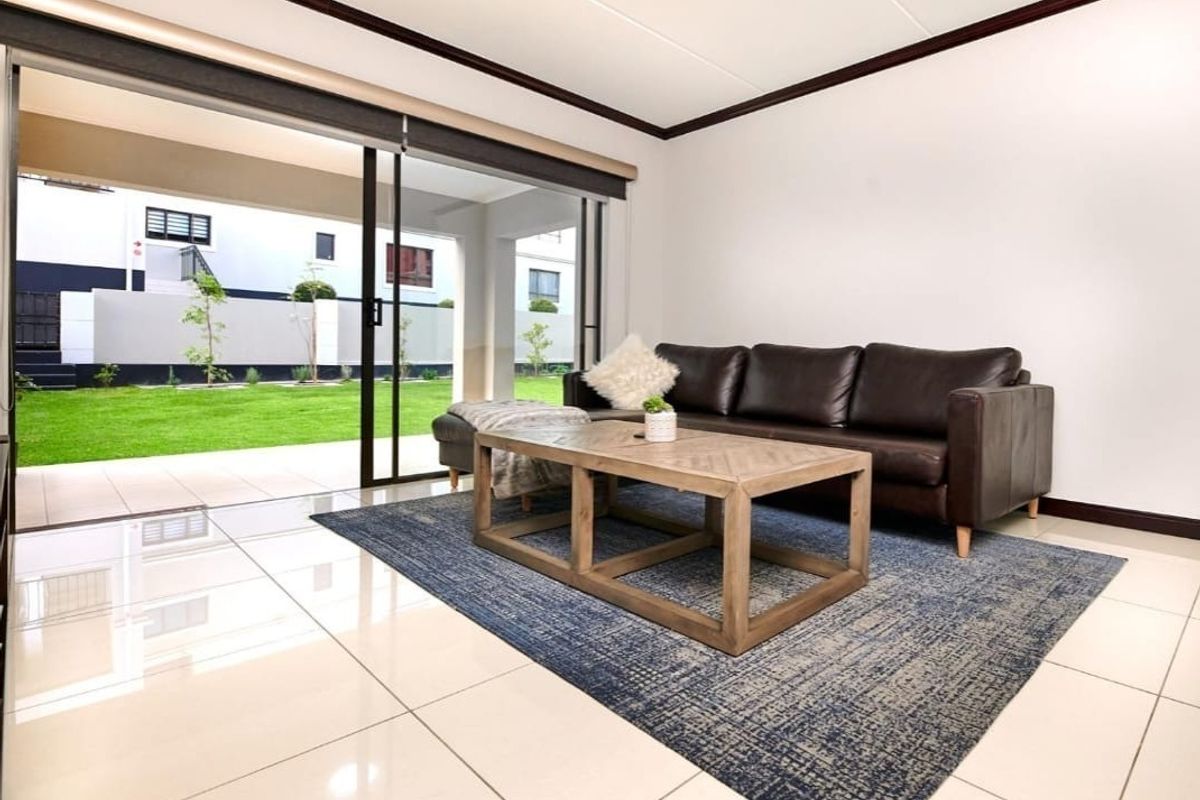 Bright living room featuring large sliding glass doors that open onto a private patio and garden area, finished with polished floor tiles.