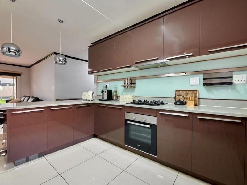 Modern kitchen featuring high-gloss brown cabinetry, stone countertops, glass splashback, and integrated stainless steel appliances, complemented by sleek tiled flooring.