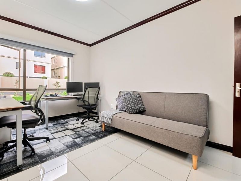 A bright and functional home office space featuring tiled flooring, crown molding, and a large window providing natural light.