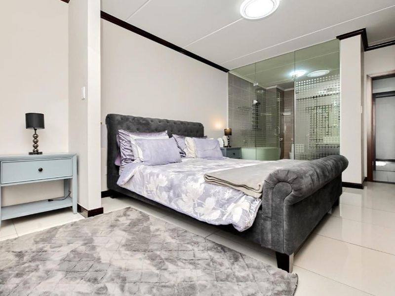 Modern bedroom featuring tiled flooring and a contemporary glass-enclosed en-suite bathroom, offering a sleek and open-plan aesthetic.