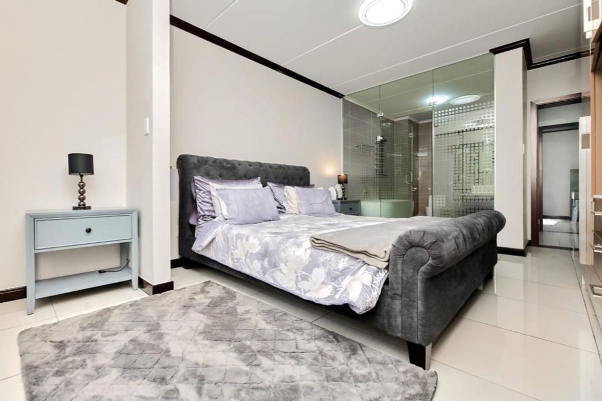 Modern bedroom featuring tiled flooring and a contemporary glass-enclosed en-suite bathroom, offering a sleek and open-plan aesthetic.