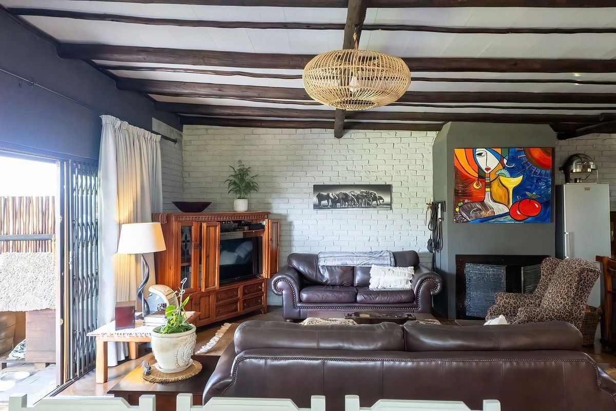 Spacious living room featuring exposed timber ceiling beams, a painted brick feature wall, and a built-in fireplace with direct access to the patio.