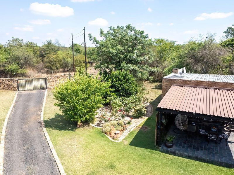 Aerial view of the property featuring a gravel driveway, gated entrance, stone boundary wall, and a covered patio area with tiled flooring.