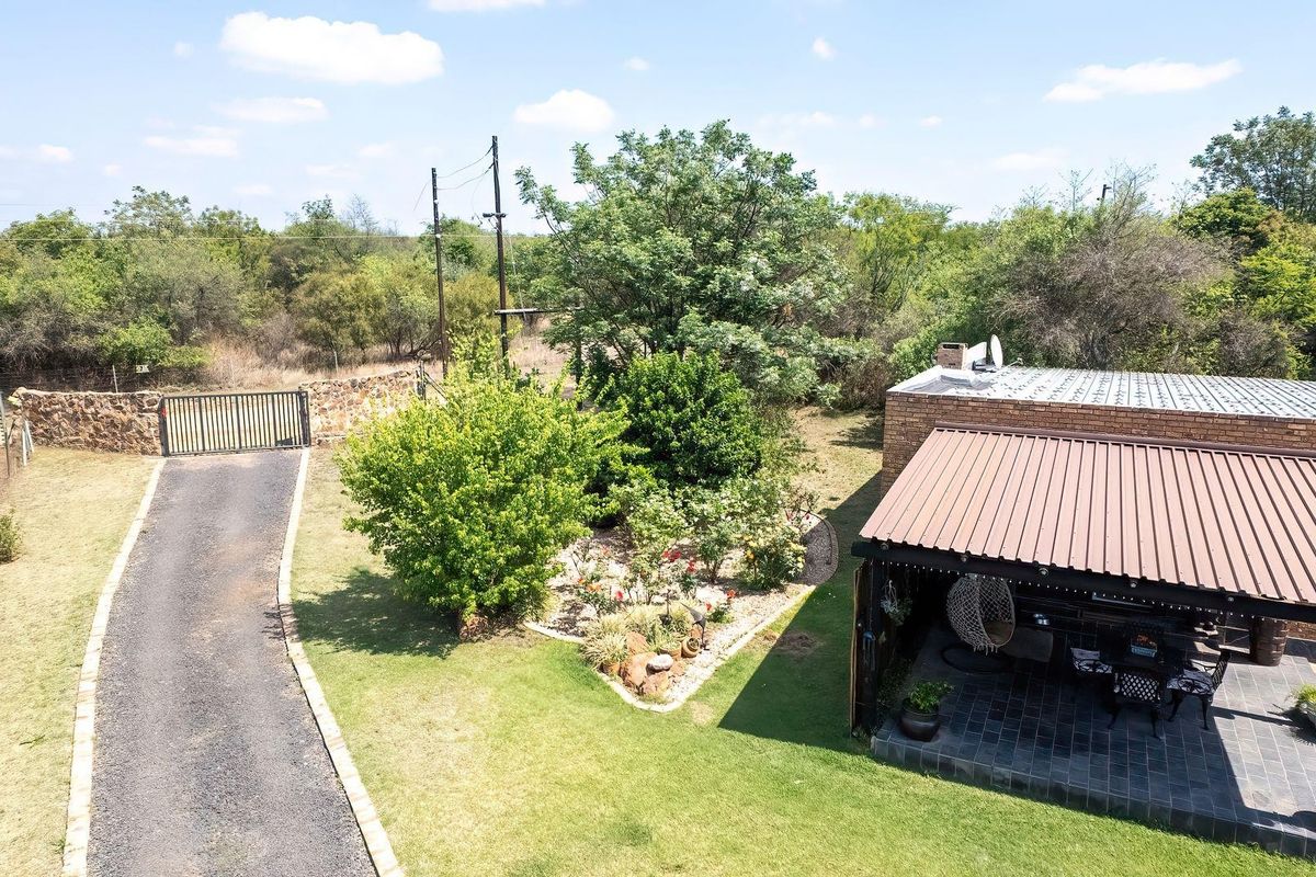 Aerial view of the property featuring a gravel driveway, gated entrance, stone boundary wall, and a covered patio area with tiled flooring.