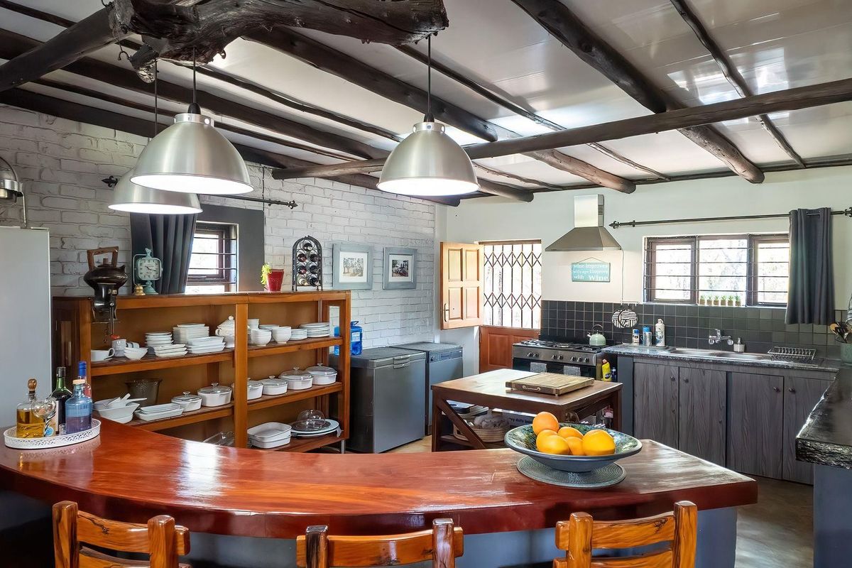 Rustic farmhouse kitchen featuring exposed timber ceiling beams, a brick feature wall, a large timber breakfast bar, and integrated gas cooking facilities.