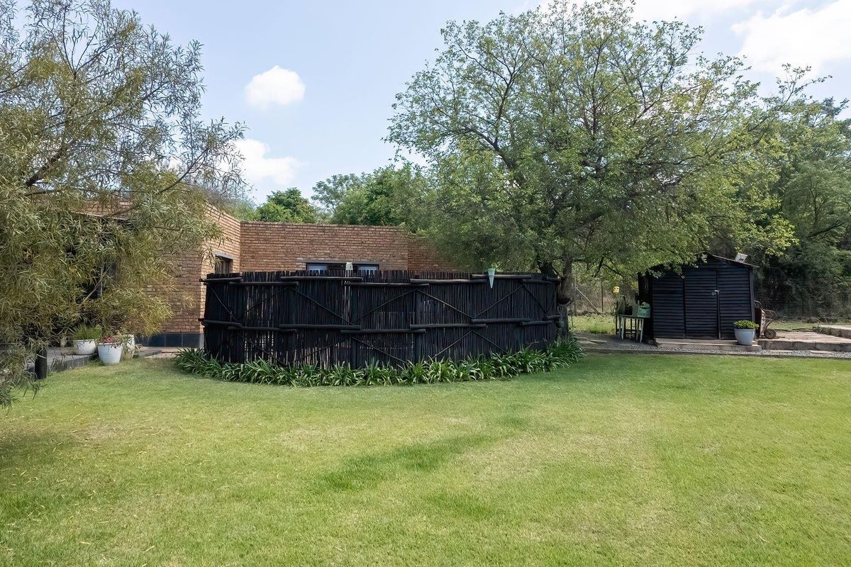 A spacious rear garden featuring a brick building facade, a decorative timber screen, and a detached storage shed set within a well-maintained lawn area.