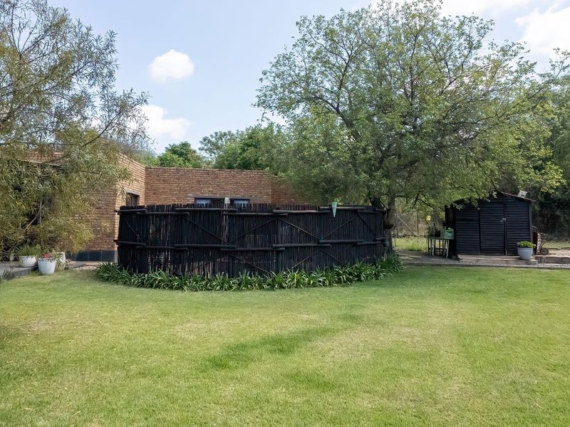 A spacious rear garden featuring a brick building facade, a decorative timber screen, and a detached storage shed set within a well-maintained lawn area.