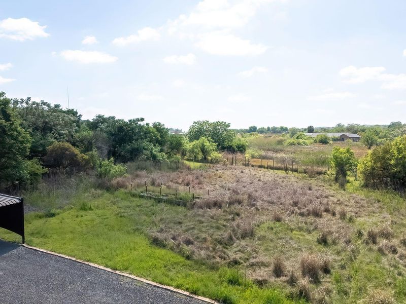 An aerial view of the property grounds featuring a gravel driveway, a covered carport, and expansive open land with natural vegetation.