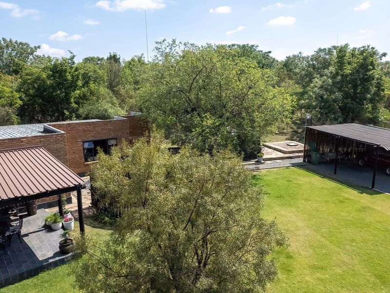 Aerial view of the farm property featuring a brick dwelling with a covered patio, a spacious lawn, and a detached carport structure.
