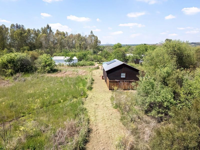 Aerial view of a timber-clad farm building featuring a metal roof with solar panels, set within a rural landscape with surrounding vegetation.