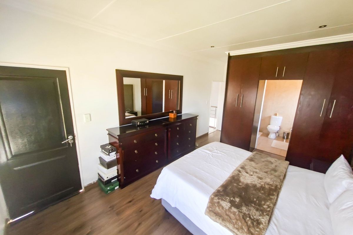 Spacious bedroom featuring dark wood built-in cupboards, laminate flooring, recessed lighting, and direct access to an en-suite bathroom.