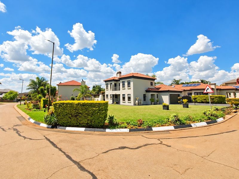 A well-maintained two-story residential property featuring a tiled roof, attached garage, and a balcony, situated on a corner lot with a landscaped front garden.
