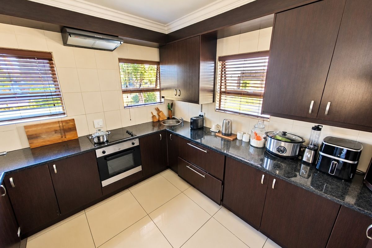 A well-maintained kitchen featuring dark wood cabinetry, granite countertops, built-in oven, electric hob, and tiled flooring with ample natural light.