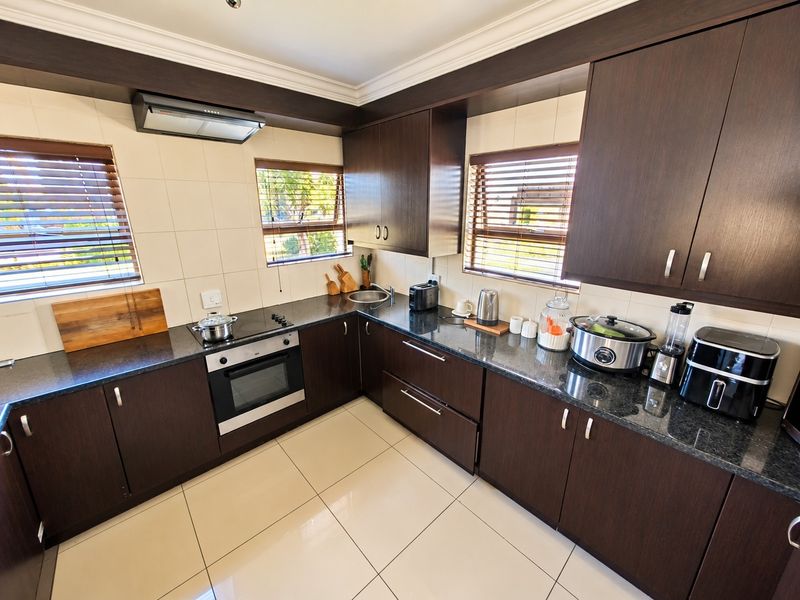A well-maintained kitchen featuring dark wood cabinetry, granite countertops, built-in oven, electric hob, and tiled flooring with ample natural light.
