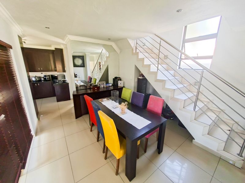 Open plan dining area featuring a modern staircase with stainless steel balustrades, tiled flooring, and an adjacent kitchen with dark cabinetry.