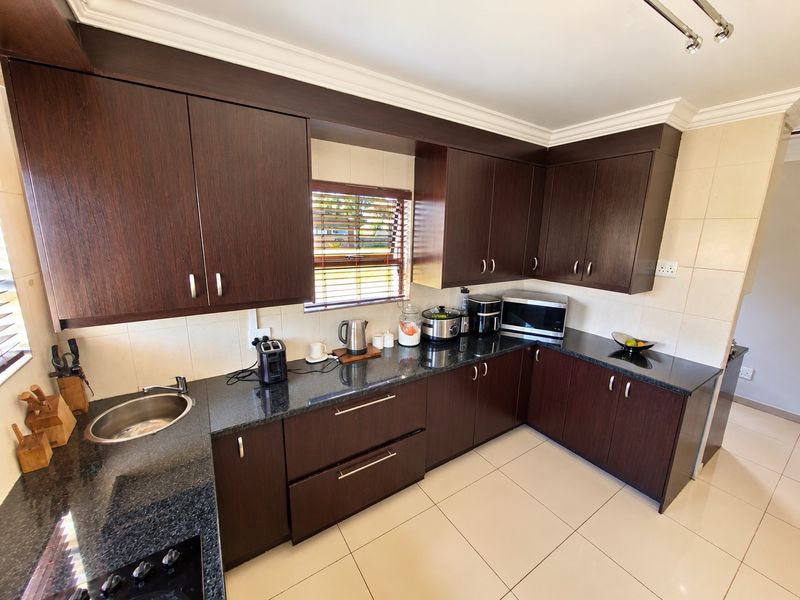 A functional kitchen featuring dark wood cabinetry, granite countertops, tiled backsplash, and ceramic flooring, offering a clean and well-maintained workspace.