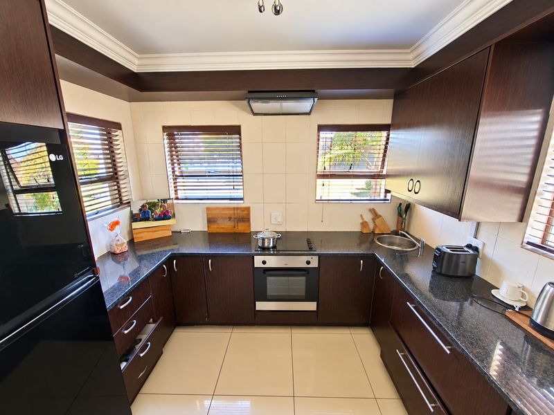 A well-maintained U-shaped kitchen featuring dark wood cabinetry, granite countertops, integrated oven and hob, and large floor tiles.