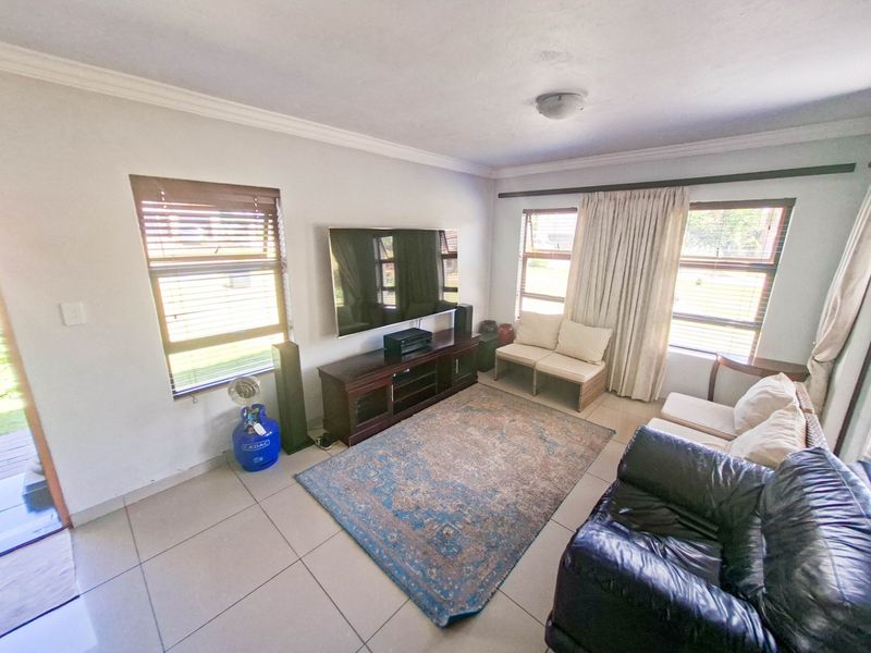 A bright living room featuring tiled flooring, cornicing, and large windows with fitted blinds and curtain rails.