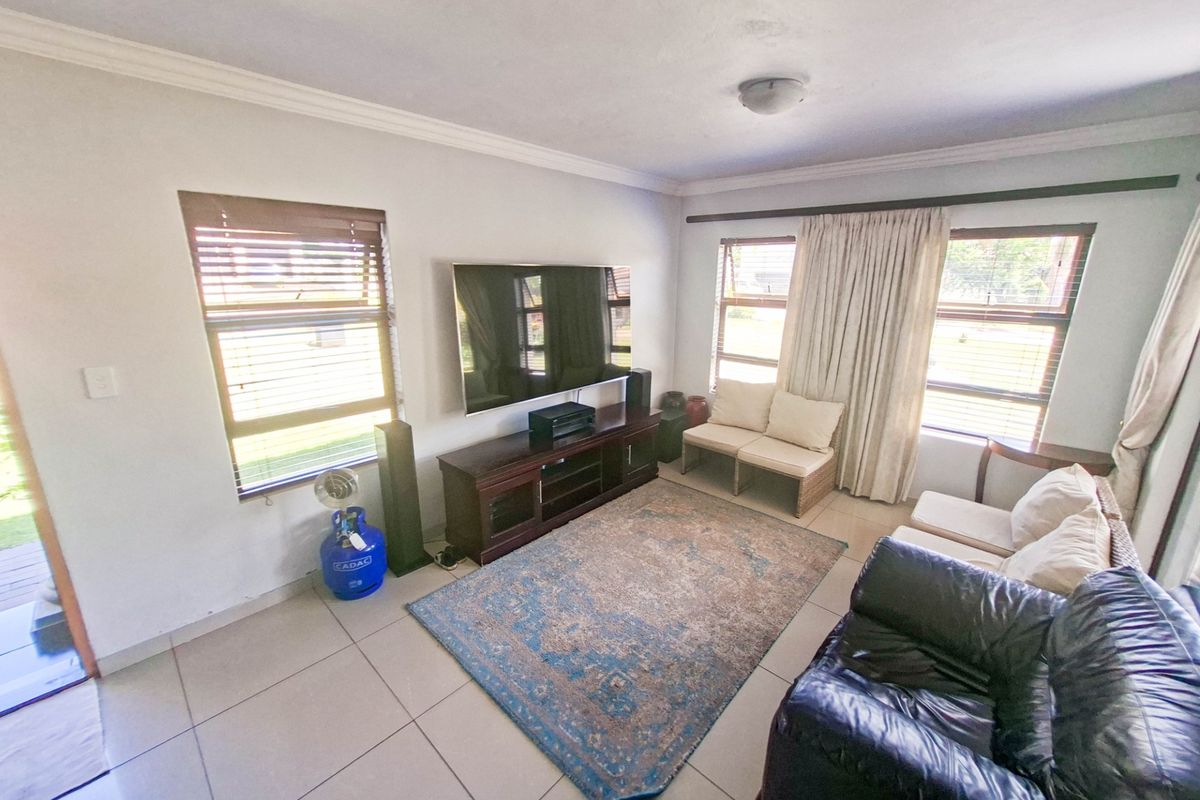 A bright living room featuring tiled flooring, cornicing, and large windows with fitted blinds and curtain rails.