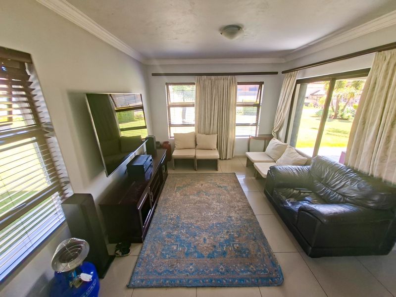 A bright living room featuring tiled flooring, large windows, and sliding glass doors that provide access to the garden area.