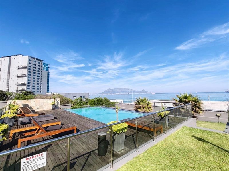 Outdoor pool area featuring timber decking, glass balustrades, and panoramic ocean and mountain views.