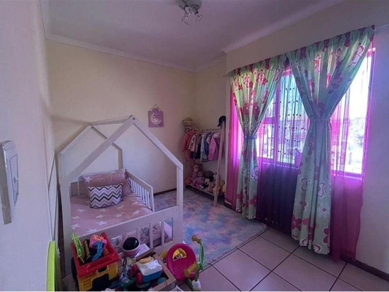 A standard bedroom featuring tiled flooring and a window with curtain fixtures, providing a functional space for a child's room.