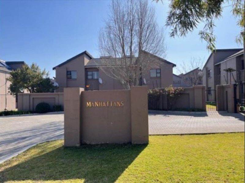 Front entrance view of the Manhattans townhouse complex featuring paved driveway access, perimeter walling, and security fencing.