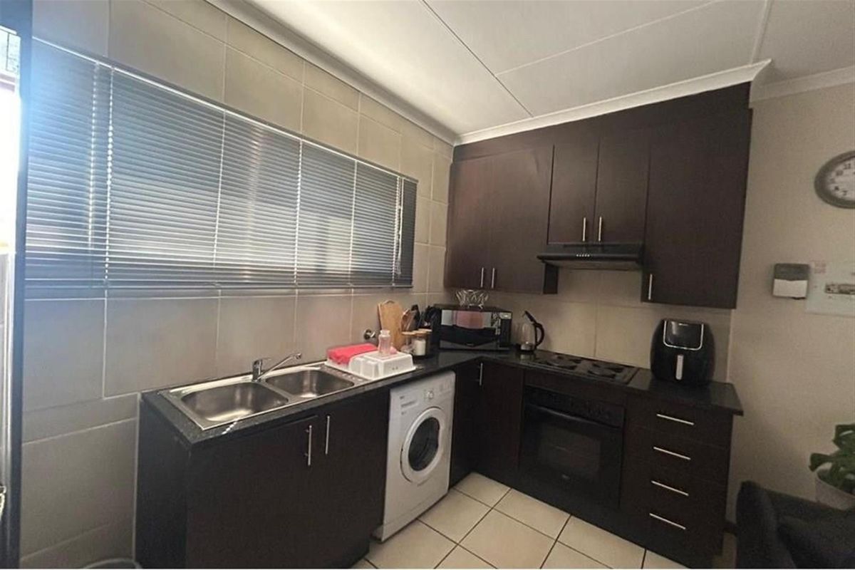 A functional kitchen featuring dark wood cabinetry, granite countertops, a double sink, and built-in cooking appliances with tiled splashbacks and flooring.