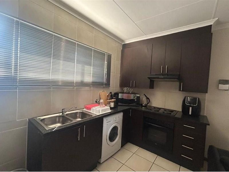A functional kitchen featuring dark wood cabinetry, granite countertops, a double sink, and built-in cooking appliances with tiled splashbacks and flooring.