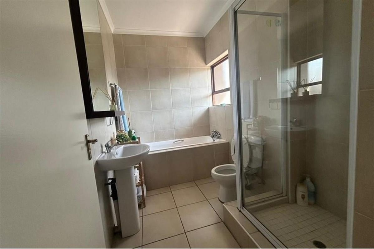 A functional bathroom featuring a pedestal basin, built-in bathtub, and a separate shower enclosure with neutral wall and floor tiling.